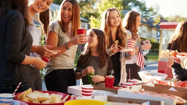 Group of people at table set ouf with picnic food on street during a neighborhood block party.